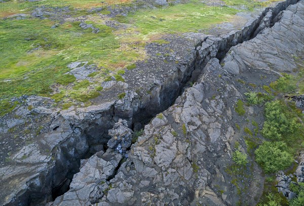 Black fissure runs through green meadow in fault zone