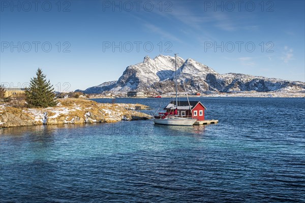 Red wooden cabin on raft with sailing boat in the sea off the coast