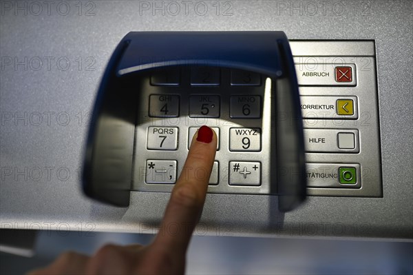 Woman typing in secret code at the cash machine of a savings bank