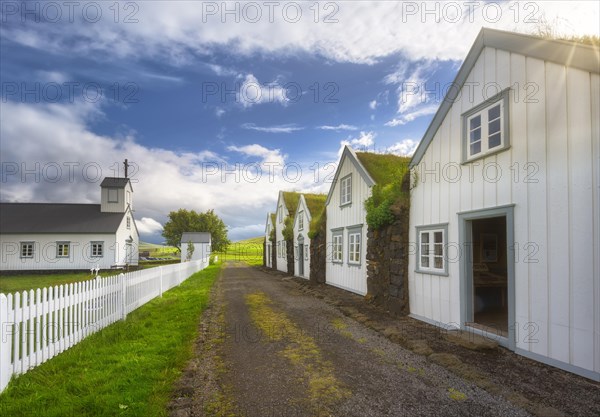 White houses with grass roof and stone wall along a gravel road