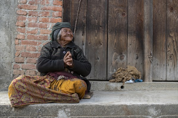 Friendly smiling elderly woman with headscarf and nose ring sitting in front of a wooden door