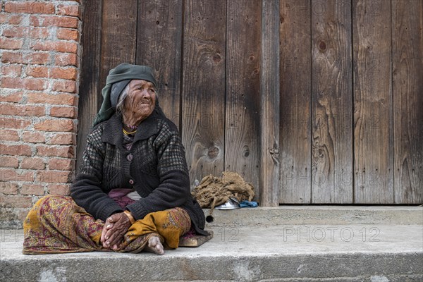 Elderly woman with headscarf and nose ring sitting in front of a wooden door