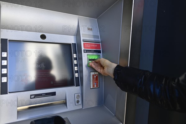 Woman waiting for the ec-card at the cash dispenser of a savings bank