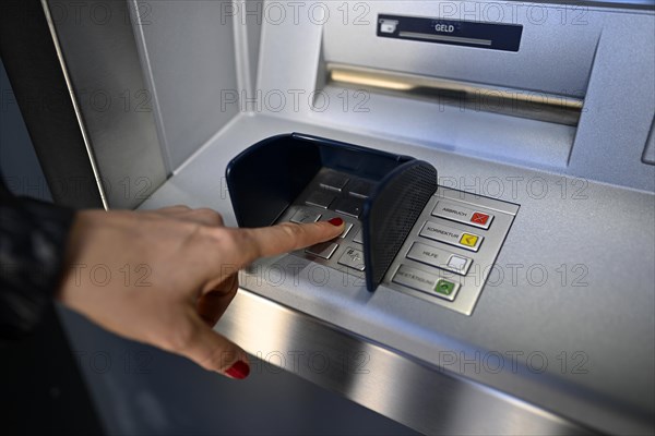 Woman typing in secret code at the cash machine of a savings bank