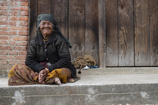Friendly smiling elderly woman with headscarf and nose ring sitting in front of a wooden door