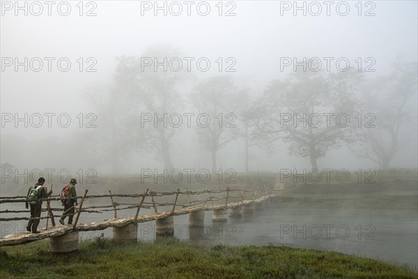Two men walk in the morning fog over a bridge over the Rapti River