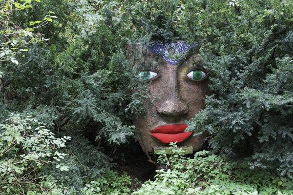 Magical woman face with red lips and green eyes looks through branches
