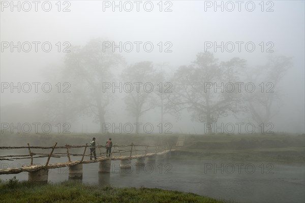 Two men walk in the morning fog over a bridge over the Rapti River