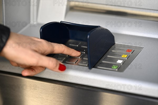 Woman typing in secret code at the cash machine of a savings bank