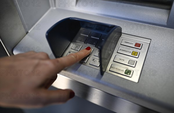 Woman typing in secret code at the cash machine of a savings bank