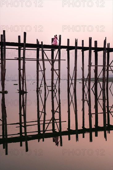 Buddhist monks walk across the U-leg bridge in pink robes as the sun rises