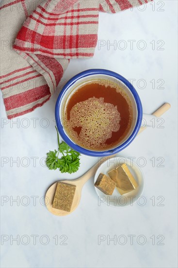 Cup with bouillon broth and bouillon cubes on a wooden spoon