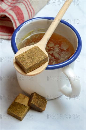 Cup with bouillon broth and bouillon cubes on a wooden spoon