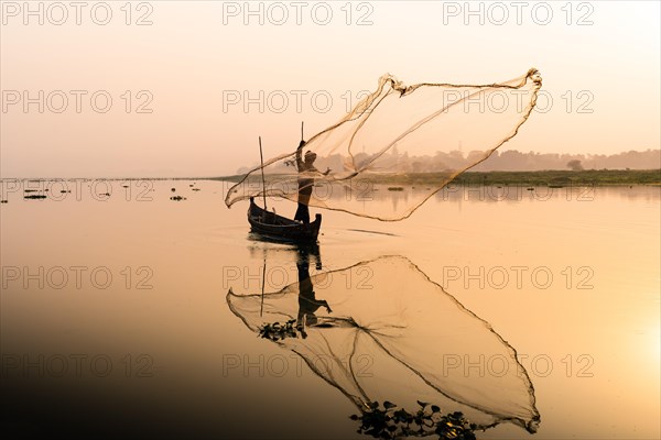 Fisherman with boat on Taung Tha Man Lake casts a fishing net for sunrise