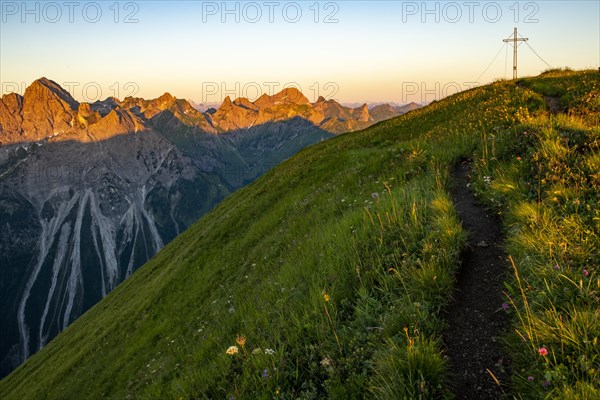 Small mountain trail with flower meadow and summit of the Uentschenspitze at sunrise