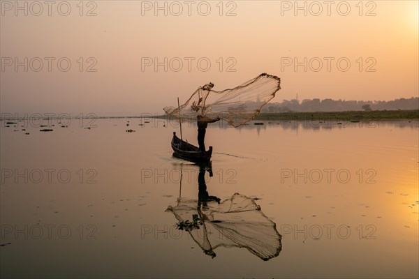 Fisherman with boat on Taung Tha Man Lake casts a fishing net for sunrise