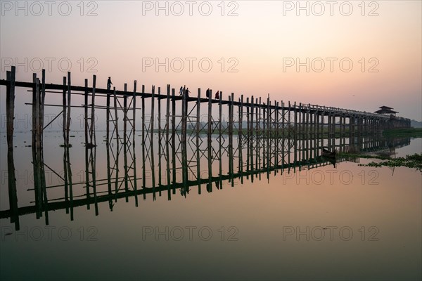 Buddhist monks walk across the U-leg bridge in red robes as the sun rises