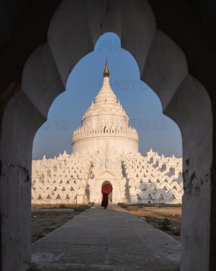 Buddhist monk stands with red umbrella in front of Hsinbyume Pagoda with frame of another pagoda