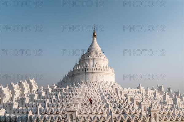 Buddhist monk stands with red umbrella in front of Hsinbyume Pagoda