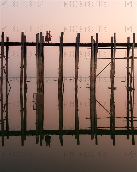 Buddhist monks walk across the U-leg bridge in red robes as the sun rises