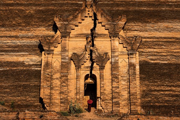 Buddhist monk stands with red umbrella in the entrance of Mingun Pagoda