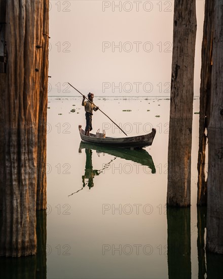 Fisherman stands with boat on Taung Tha Man Lake for sunrise between the posts of the U-leg bridge