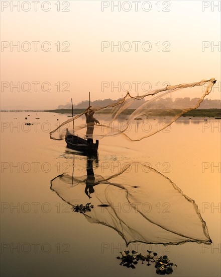 Fisherman with boat on Taung Tha Man Lake casts a fishing net for sunrise