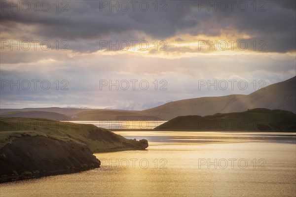 Sun breaks through clouds at the lake with hills