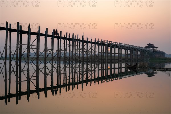 Buddhist monks walk across the U-leg bridge in red robes as the sun rises