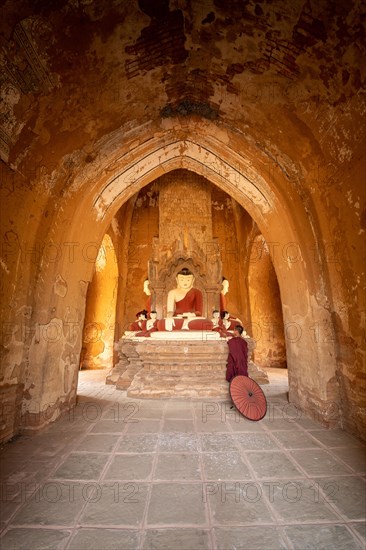 Buddhist young monk in red robe with red umbrella standing in a temple and praying