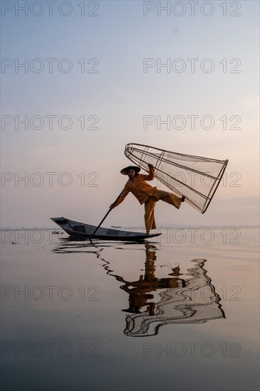 Traditional fisherman posing standing on his small boat with reflection in front of sunrise