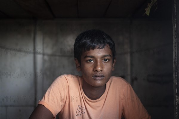A sailor is sitting at the entrance of his sleeping cabin on a freighter in the port of Mongla