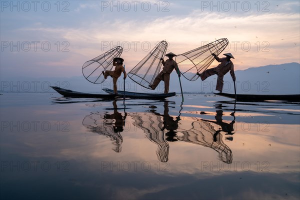 Three traditional fishermen pose standing on their small boats