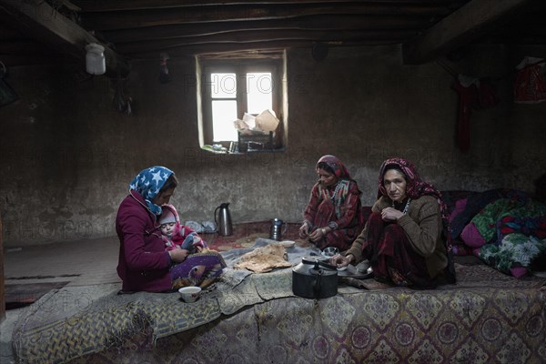 A woman with an infant and two other woman sitting on carpets in the living room of a traditional mud house