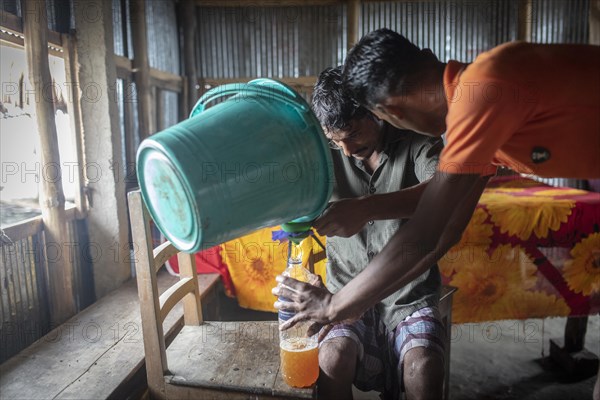 Honey collectors fill nectar from a bucket into plastic bottles