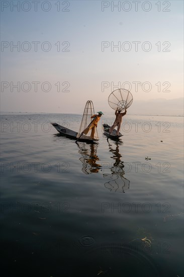 Two traditional fishermen pose standing on their small boats