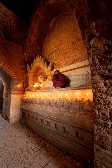 Buddhist young monk in red robe with red umbrella praying with candle in hand in a temple