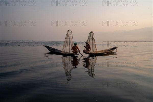 Two traditional fishermen pose sitting on their small boats