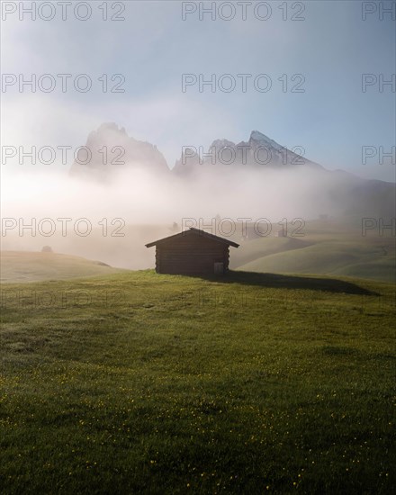 Hay barn and huts on foggy meadows in front of Sassolungo and Plattkofel