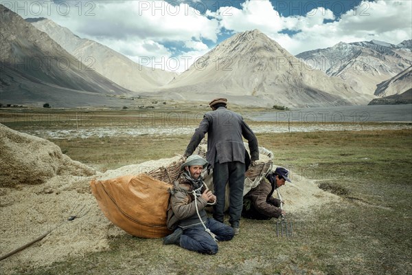 One man helps two other men shoulder their baskets of wheat to bring the harvest from the fields to the granaries