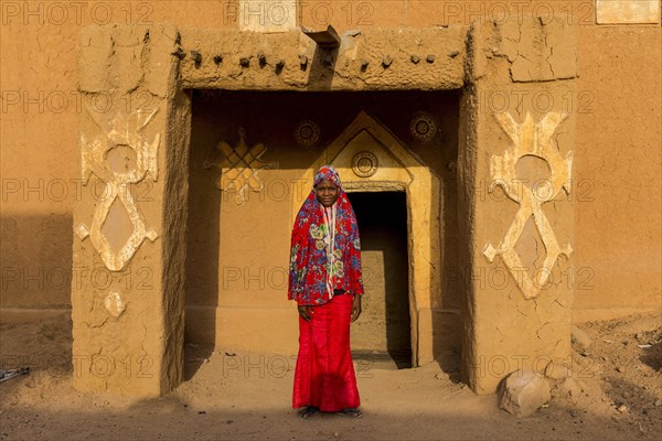 Young girl in traditional clothing in front of a mud house