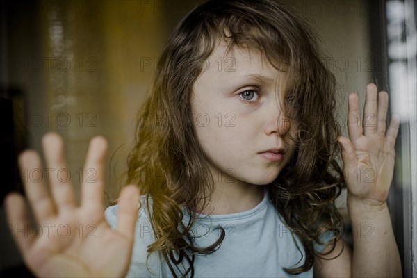 Child looks sadly through window pane