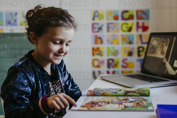 Little girl learning with reading book and laptop