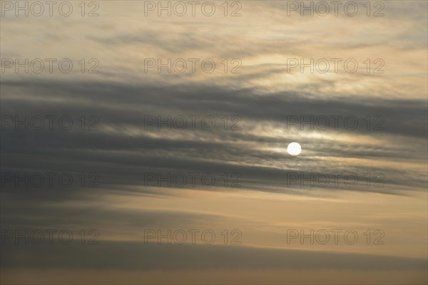 Sun shines behind layered clouds
