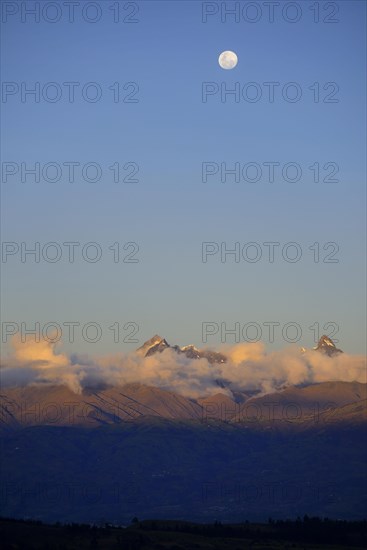 Mountain peak of the Andes above a cloud bank with full moon