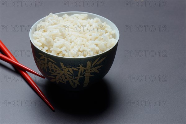 Boiled rice in bowl with chopsticks