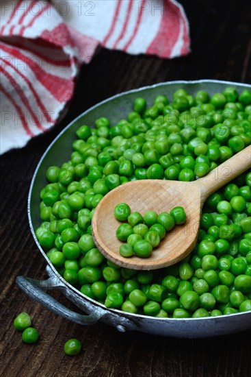 Defrosted green peas in shell with cooking spoon