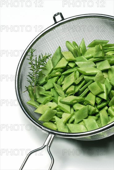 Sliced broad beans with savory in kitchen sieve