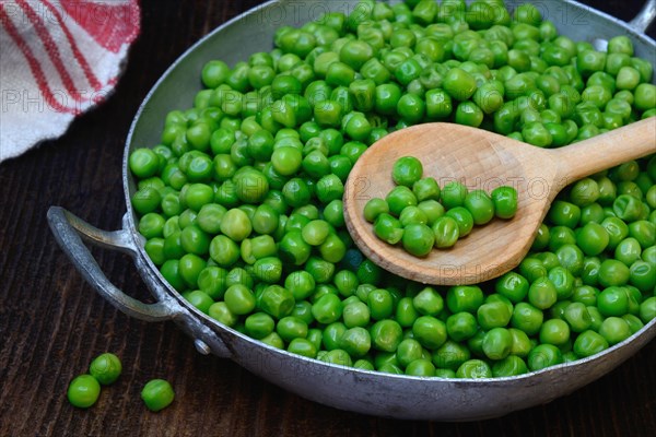 Defrosted green peas in shell with cooking spoon