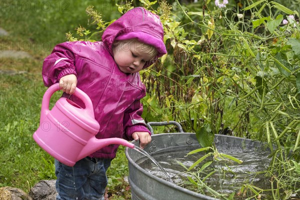 Little girl with rubber boots and rain jacket playing with water and watering can in the rain